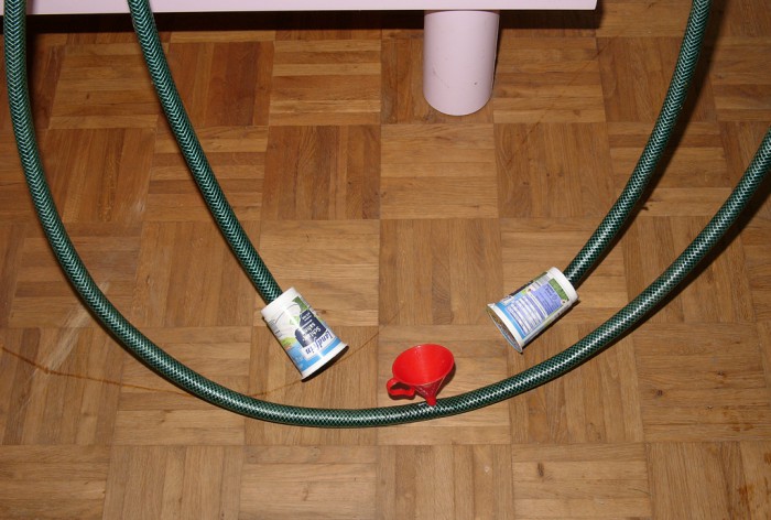 In der Mitte des Schlauchs wurde ein Trichter gesteckt, danach die &quot;Versuchsanlage&quot; blasenfrei mit Wasser gefüllt und waagrecht ausgelegt. . .